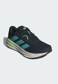 Baskets de course navy avec dessus en mesh, accents verts et bleu clair, branding à trois rayures et une semelle blanche rembourrée.