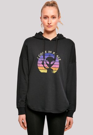 Schwarzer Hoodie mit lässigem Schnitt, der ein buntes Alien-Graphic in einem kreisförmigen Design und den Text "ICH KOMME IM FRIEDEN" zeigt. Kapuze mit Kordelzug.