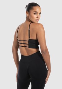 Zwarte geribbelde bralette met dunne bandjes en een gekruist rugontwerp, gecombineerd met hoge zwarte leggings. Gladde textuur en aansluitende pasvorm.