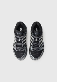 Černé sportovní boty s horní částí z mesh materiálu, stříbrnými akcenty a šedými tkaničkami. Mají texturovanou podešev a zesílenou špičku pro větší odolnost.