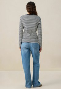 Zwart-wit gestreepte top met lange mouwen, gecombineerd met losse blauwe jeans. Ontspannen pasvorm met een ronde halslijn en een eenvoudige achterkant.
