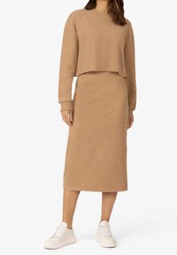 Ensemble en tricot khaki à deux pièces comprenant un pull court avec des poignets côtelés et une jupe midi assortie, associé à des baskets blanches.