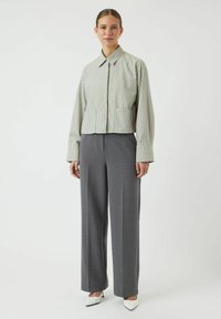 Afdæmpet, lysegrøn stribet jakke med lange ærmer og krave, parret med grå, vide bukser og hvide spidse hæle.