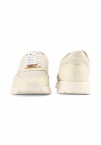 Sneakers w off-white skórze, z białymi sznurówkami i złotym akcentem na języku. Gładka tekstura z amortyzującą podeszwą.