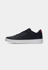 Baskets basses bleu marine avec semelle blanche, fermeture à lacets, détail de talon rouge et petit logo Tommy Hilfiger sur le côté.