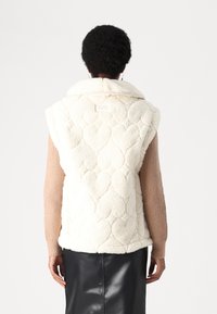 Vit, fluffig väst med hjärtformad quiltad mönster och krage, tillsammans med en strukturerad beige långärmad topp och en svart kjol.