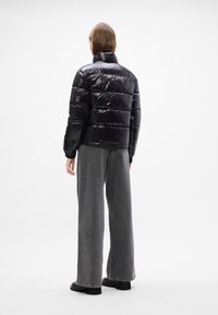 Melna, spīdīga pūka jaka ar pāršūtiem paneļiem un augstu apkakli; kombinēta ar brīvām pelēkajām džinsām un masīvām melnām zābakām.