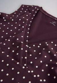 Purple sleeveless dress with white polka dots and a V-neckline laid flat on a light surface.