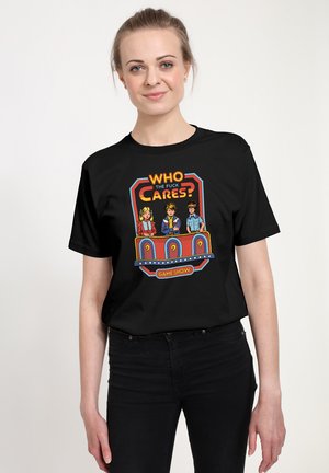T-shirt en coton noir arborant un graphique coloré d'un jeu télévisé avec trois personnages de dessin animé et le texte "QUI S'EN FOUS ?"