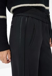 Pantalons de sport noirs avec une taille texturée, des poches latérales et des rayures lisses contrastantes le long des coutures. Conviennent pour le port décontracté.