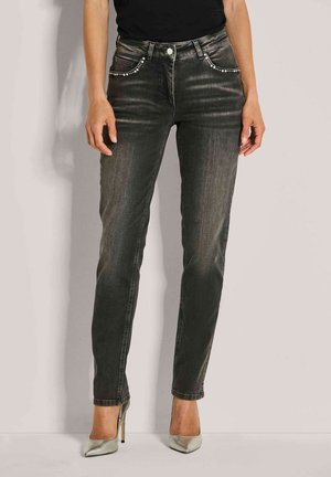 Frau in verblassten schwarzen Slim-Fit-Jeans mit Strassakzenten an den Fronttaschen und silbernen High-Heels.