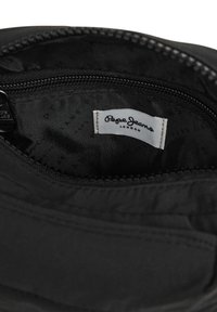Interno nero di una borsa con una cerniera. L'etichetta in evidenza riporta "Pepe Jeans London." Texture liscia, design minimalista, nessun motivo visibile.