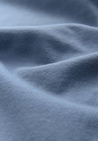 Bavlnená látka v jemnej modrej farbe s hladkou textúrou a jemným rebrovaným vzorom, so šetrnými záhybmi a plynulými líniami závesu.