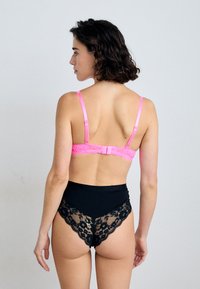 Rosa Spitze-BH mit verstellbaren Trägern und Hakenverschluss, kombiniert mit schwarzen hochgeschnittenen Panties, die mit schwarzem Spitzenbesatz und floralen Mustern verziert sind.