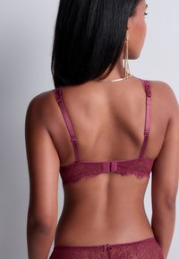 Bralette en dentelle bourgogne avec une bande satinée lisse, des bretelles réglables et une fermeture à crochet à l'arrière. Détails en dentelle complexes le long des bords.