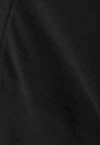 Un tissu noir avec un motif texturé délicat, comportant des sections lisses et côtelées, mettant en valeur un design élégant et moderne.