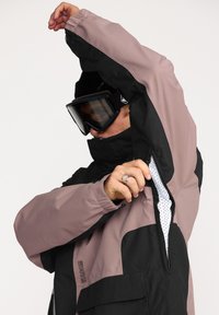 Sneeuwjack met een zwart en mauve kleurenschema, voorzien van ritsventilatieopeningen, een hoge kraag en elastische manchetten voor bescherming tegen het weer.