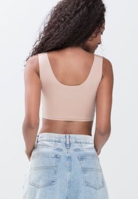 Lysebrune cropped tanktop med brede stropper, glat tekstur og en rund rygudskæring, parret med high-waisted denimshorts.