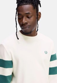 Sudadera beige con mangas a rayas verdes, cuello de canalé y pequeño logotipo verde en el pecho. Fabricada con una suave tela texturizada.