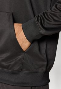 Sort træningshoodie med en blød, glat tekstur, ribbede manschetter og en frontlomme, med en afslappet pasform og minimalistisk design.
