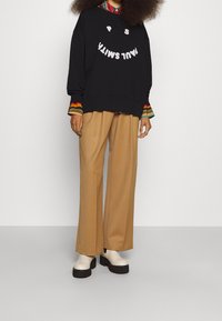 Sudadera negra de corte holgado, con el texto blanco "P S M I L T A", combinada con pantalones anchos color crema y zapatillas de plataforma blancas.