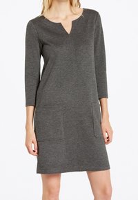 Robe en tricot grise avec un col en V, des manches trois-quarts et deux poches avant. Design simple avec une silhouette droite et une texture douce.