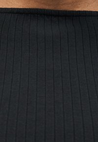 Κοντινό πλάνο μαύρου ριμπ ύφανσης με κάθετες γραμμές και ένα μικρό τμήμα δέρματος ορατό στην επάνω άκρη.