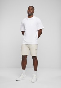 Hvit T-skjorte med kort erm og beige cargo-shorts, med to sidelommer. Stylet med hvite sneakers og hvite ankelsokker.
