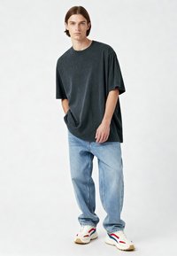 Per didelį anglies spalvos medvilnės marškinėlį trumpomis rankovėmis, derinamą su šviesiai mėlynomis plačiomis džinsomis ir baltais sportbačiais su raudonais ir mėlynais akcentais.