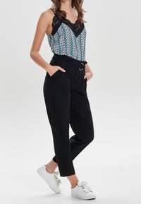 Svarta högmidjade byxor med sidofickor och bältesslingor, i kombination med en mönstrad linne med spetsdetaljer och V-ringning.