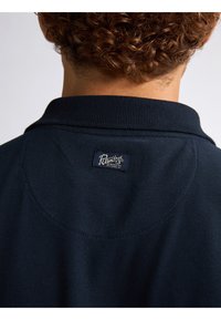 Marineblauwe poloshirt met een gestructureerde stof, korte kraag en een label op de nek met het merk "Petrolind 73".