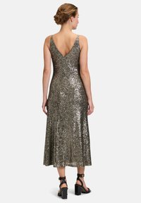 Robe en sequins argentés métalliques avec un dos en V, un corsage ajusté et une jupe évasée. Des sandales noires à talons épais complètent la tenue.