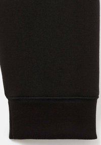Dettaglio della gamba dei pantaloni felpati neri in cotone, caratterizzato da una texture liscia, polsini a coste e orlo cucito per una maggiore durevolezza.