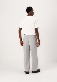 Weißes T-Shirt mit kurzen Ärmeln und hellgraue, locker sitzende Hose mit elastischem Bund. Die Rückansicht zeigt flache Taschen und schwarze Schuhe.