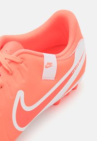 Bright coral Nike Tiempo football boot with a textured synthetic upper, white logo, and contrasting white accents, designed for traction.