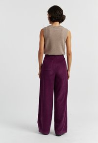 Beige mouwloos topje met ribbelnek, gecombineerd met hoge taille, wijdvallende paarse corduroy broek met details op de achterzak.