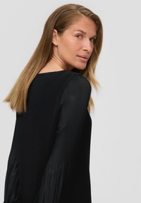 Schwarzes geripptes Oberteil mit langen, fließenden Ärmeln und einem quadratischen Ausschnitt. Es hat eine weiche Textur und ein tailliertes Oberteil, das eine elegante Silhouette betont.