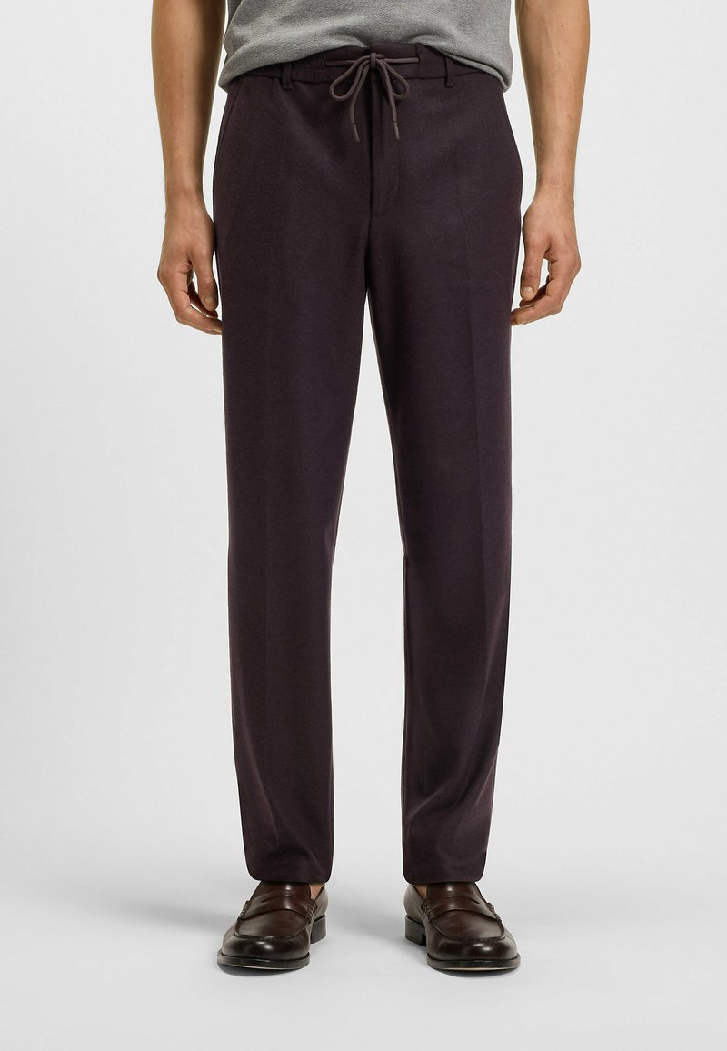 Mörklila byxor med avslappnad passform, dragsko i midjan och smidig textur, kombinerat med bruna loafers.