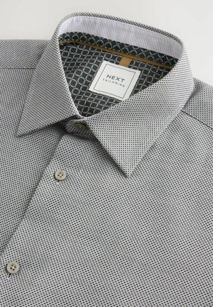 Men's shirt in a black and white micro-pattern, featuring a structured collar, beige buttons, and a contrasting geometric inner collar lining.