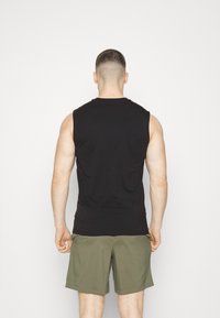 Débardeur noir en coton, avec un col arrondi et une coupe décontractée, associé à un short vert olive.