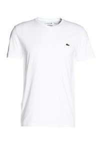 T-shirt en coton blanc avec col en V et manches courtes. Présente un petit logo crocodile vert brodé sur la partie gauche de la poitrine.