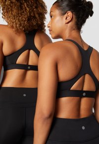 Sutiãs desportivos pretos com um design de costas recortadas apresentam uma faixa sólida e um detalhe do logo de estrela, acompanhados de leggings de cintura alta pretas a condizer.
