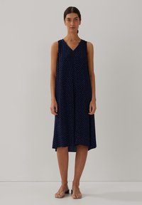Marineblaues ärmelloses Kleid mit kleinen weißen Punkten, V-Ausschnitt, fließender Silhouette und weichem Stoff, der gerade unter dem Knie endet.