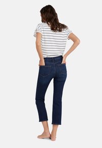 Jeans denim berwarna biru tua dengan gaya yang pas, dilengkapi dengan saku belakang dan panjang yang dipotong. Dipasangkan dengan atasan lengan pendek bergaris putih.