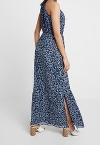 Maxiklänning i marinblått med blommönster, med en slits på sidan, ärmlös design och en cinchad midja. Slät, lättviktigt tyg.