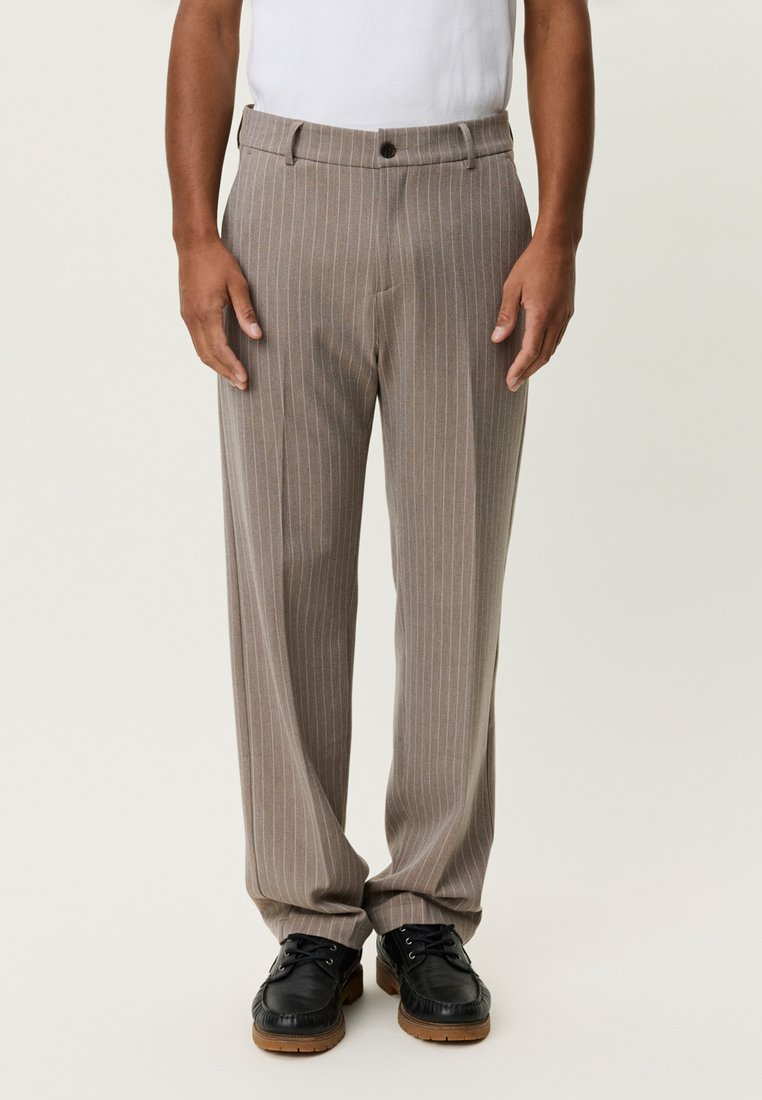 Μπεζ παντελόνι με λωρίδες, κομμένο ίσια, με κουμπιά και πλαϊνές τσέπες. Συνδυασμένο με μαύρα παπούτσια με κορδόνια.