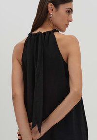 Top nero con scollo halter, caratterizzato da un collo arricciato, con una vestibilità ampia e un elegante dettaglio a nacchera sul retro. Design semplice e minimal.