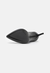 Chaussure à talon haut noire à bout pointu, couchée sur le côté, montrant une semelle lisse avec le logo Calvin Klein près de la voûte plantaire.