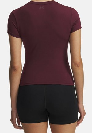 Kobieta w dopasowanej bordowej koszulce z krótkim rękawem i czarnych szortach, pokazana od tyłu na białym tle.