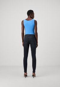 Kék ujjatlan felső, kerek kivágással, sötét, skinny farmernadrággal párosítva, hátul zsebekkel és sima denim textúrával.